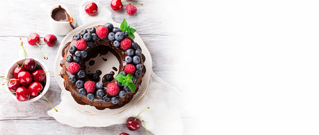 Homemade Vegan Gluten free Chocolate Cake with fresh berries - raspberry, blueberry and cherry on white wooden table. Healthy Food, Gluten Free Food Concept.