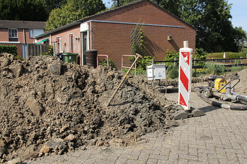 Hulst, Holland - sep 12, 2022: a heap of sand with a shovel and flexible poles in the streets during ground works for cables and pipes