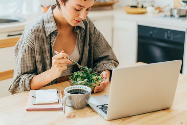 istock Young modern business woman eats salad while sitting in the kitchen with a computer. 1432680752