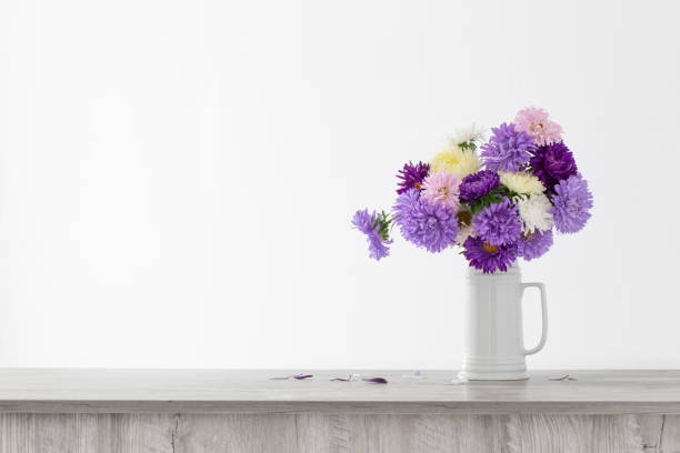 beautiful bouquet of asters in white jug on background white wall