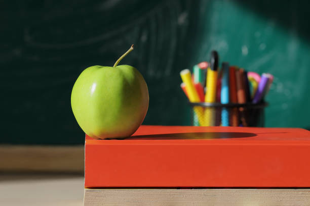 istock Green apple on a stack of books in a school classroom. Selective focus. 1432688943