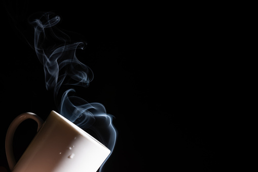 A white cup against a black background with smoke coming out of it. Close up. Porcelain stuff.