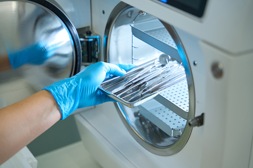 Woman hand in blue medical gloves puts a dental instrument into the sterilization apparatus