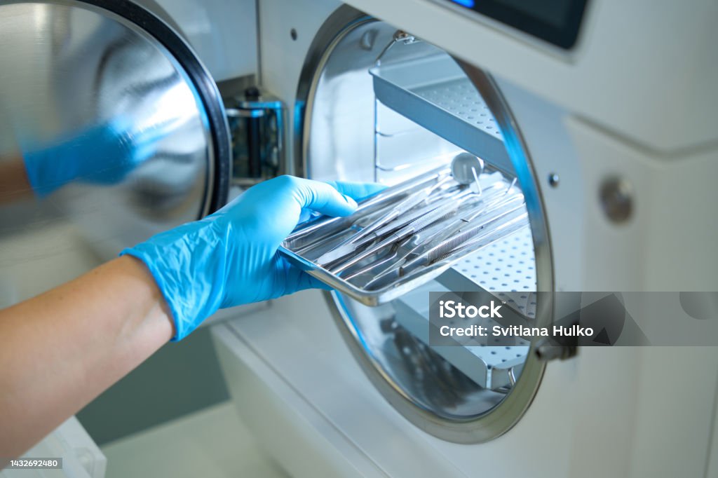 Woman hand in gloves puts dental instrument into sterilization apparatus Woman hand in blue medical gloves puts a dental instrument into the sterilization apparatus Disinfection Stock Photo
