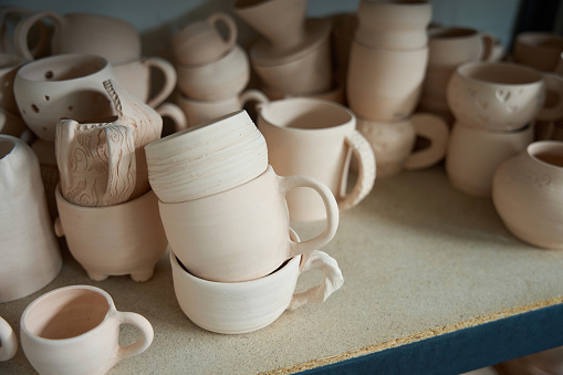 Variety of unfinished earthenware cups stand on a simple wooden shelving unit
