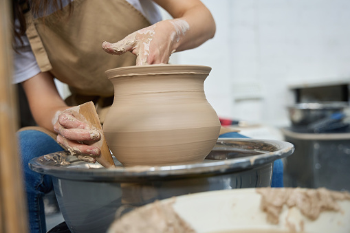 Female potter with skillful hands forms a clay product on a potter wheel