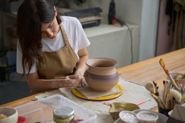 istock Craftswoman sits at table and works with spatula on clay vase 1432692673