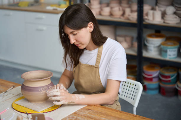 istock Craftswoman sits at her workplace and draws pattern on pot 1432692679
