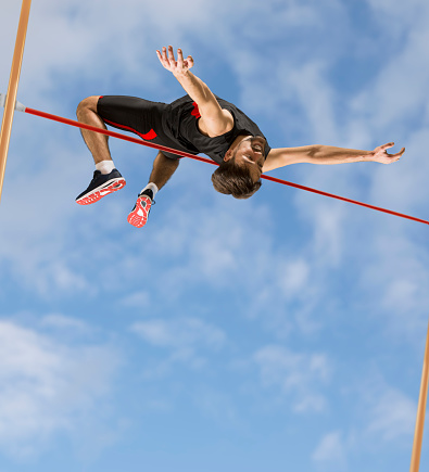 Young athlete doing high jump in sports hall during practice.