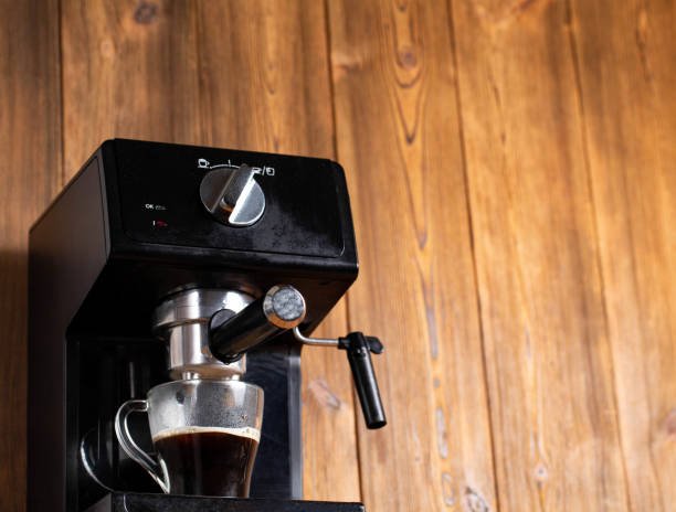 istock Making coffee in a coffee machine in the kitchen, close-up. Black coffee flowing into a transparent cup on a wooden table top background. Copy space for text 1432697238