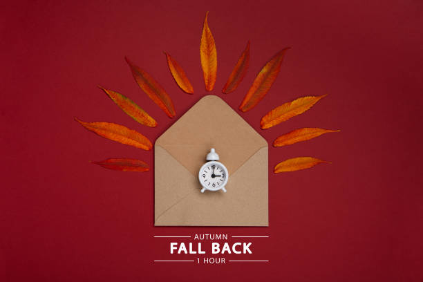 istock Fall Back, Autumn Time Change Concept. White Alarm Clock and Orange Autumn Leaves on Red Background. 1432699702