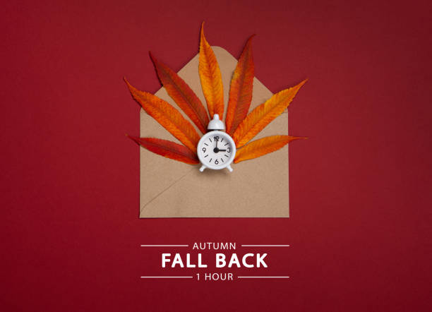 istock Fall Back, Autumn Time Change Concept. White Alarm Clock and Orange Autumn Leaves on Red Background. 1432699727