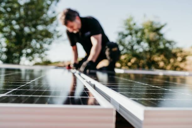 mature Technician man assembling solar panels on house roof for self consumption energy. Renewable energies and green energy concept. focus on foreground stock photo