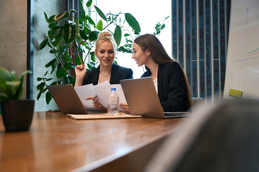 Two smiling company employees with documents in hands sitting at office desk