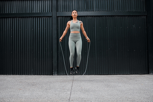 One young african american female athlete skipping using jump rope while exercising outside in the city. Beautiful and dedicated mixed race sportswoman working out alone against an urban background