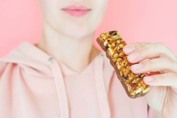 istock Young woman holding protein bar close-up on pink background, selective focus. 1432702170