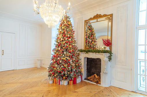 Classic Christmas decorated interior room, New year tree with red and gold decorations. Modern white classical style interior design apartment with fireplace and Christmas tree. Christmas eve at home