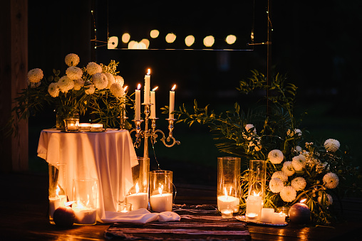 Romantic candlelight dinner at terrace restaurant at night. Location for surprise marriage proposal. A place for date or engagement in park in a tent and decorated with candles and garlands. Closeup.