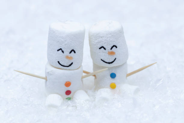 A pair of marshmallow snowmen sit in the snow. stock photo