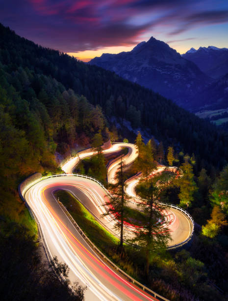 The mountain pass of Maloja, Switzerland. A road with many curves among the forest. A blur of car lights. Landscape in evening time. Large resolution photo for travel The mountain pass of Maloja, Switzerland. A road with many curves among the forest. A blur of car lights. Landscape in evening time. Large resolution photo for travel maloja region stock pictures, royalty-free photos & images