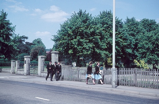 London, England, UK, 1960. Street scene with passers-by in school uniform at the edge of a London park.