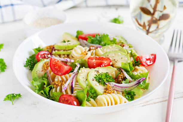 istock Fusilli pasta salad with avocado, tomatoes, fresh green lettuce, red onion and mustard dressing on white background. Vegetarian healthy lunch. 1432708176