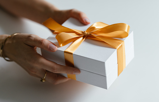 Zoomed in photo of unrecognizable woman holding a white present box with orange ribbon. Birthday or Christmas gift concept.