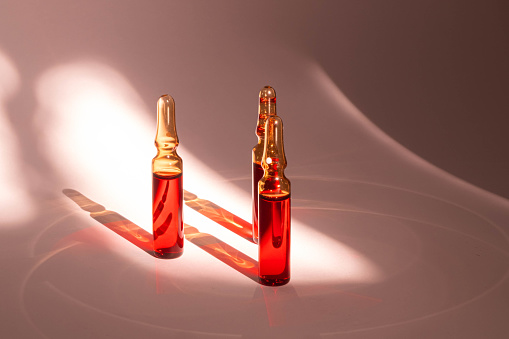 injections of B vitamins. Ampoules with red liquid on a beige background. Beauty and health concept. copy space. Blur and selective focus