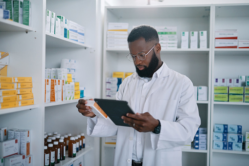 Pharmacist with digital tablet and medicine for online checklist in medical storage with pills. Black man, doctor or healthcare expert working in pharmacy retail store to check stock or product