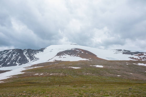 Dramatic landscape with large snowy mountain dome in sunlight under cloudy sky. Colorful scenery with sunlit high snow mountain in dome shape in center at changeable weather. Scenic mountains view. paisaje dramático con gran cúpula de montaña nevada a la luz del sol bajo un cielo nublado. paisaje colorido con alta montaña de nieve iluminada por el sol en forma de cúpula en el centro en clima cambiante. vista panorámica de las montañas.