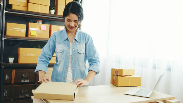 Woman packing box on table checking goods package delivery shipping to customer. Asian woman startup small business at home office desk. Entrepreneur asian woman packing product for delivery items stock photo