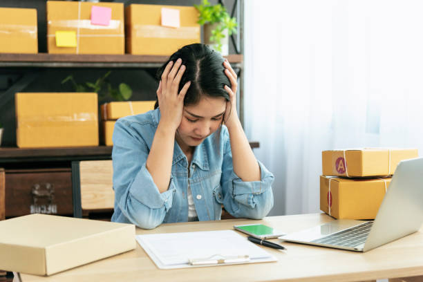 Desperate Asian woman stress headache depressed from startup small business at home office. Failure business woman work at home office. Online seller entrepreneur has problem delivery unhappy job stock photo