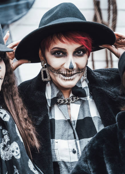 istock Scary family, mother, daughters celebrating halloween. Terrifying black skull half-face makeup and witch costumes, stylish images.Horror,fun at children's party in barn on street.Hats,jackets 1432738265