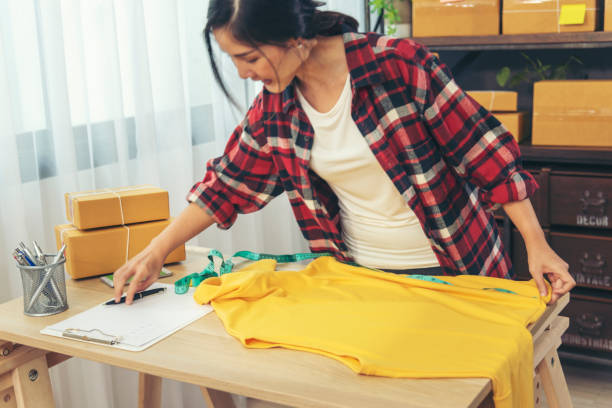 diseñadora de moda las mujeres miden la caja de embalaje de diseño de ropa en la mesa. mujeres que verifican el tamaño de los productos, la calidad del paquete de la caja de entrega. emprendedora asiática mujer startup pequeña empresa en el escritorio - selling merchandise craft thailand fotografías e imágenes de stock
