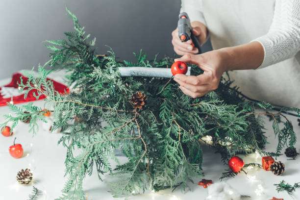 istock Florist woman makes Christmas composition for table decoration from thuja, spruce branches in wooden box. Using of floral foam, cones, snow apples, balls, cotton flowers,garland. New Year celebration 1432738314