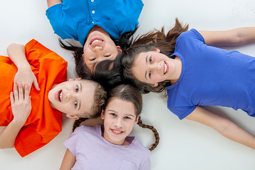 Four teenagers lay on the floor as they smile for the camera.  They are each dressed casually in this aerial view.