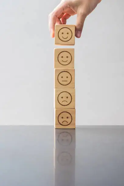 Photo of Man hand holding emotion face block. Customer choose Emoticon for user reviews. Service rating, ranking, customer review, satisfaction, evaluation and feedback concept