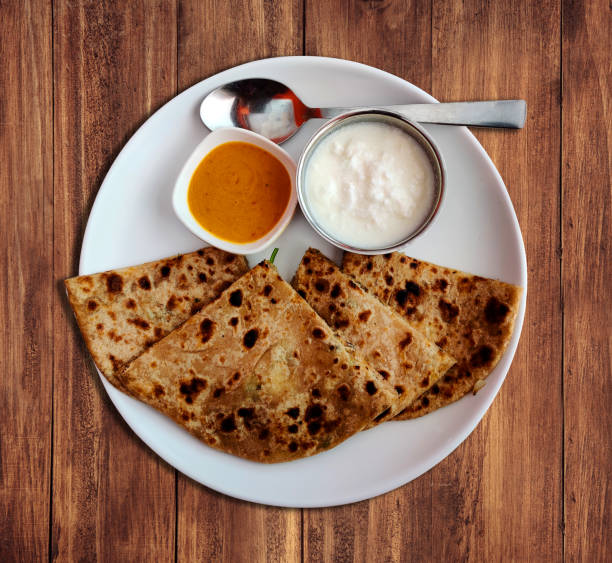 Aloo paratha or potato stuffed flat bread on a wooden background. Served with curd and sauce. Breakfast and evening snacks. stock photo