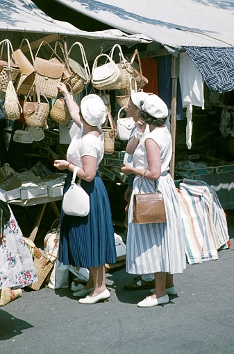 Luino, Largo de Maggiore, Lombardy, Italy, 1958. Vacationers from central Europe look at wicker handbags at a market stall.