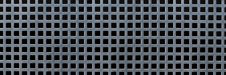 Perforated grid of gray metal with square holes against black background in panoramic close-up