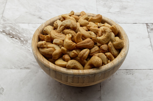 Cashew nuts in a wooden bowl isolated on clear marble background