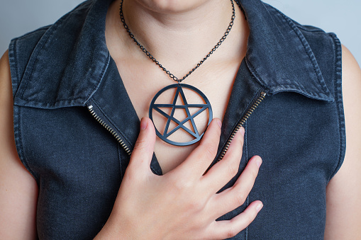 Woman in black denim dress wearing a large pentagram necklace isolate on gray.