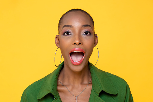 Headshot portrait of fashionable African American woman gasping in studio yellow color isolated background