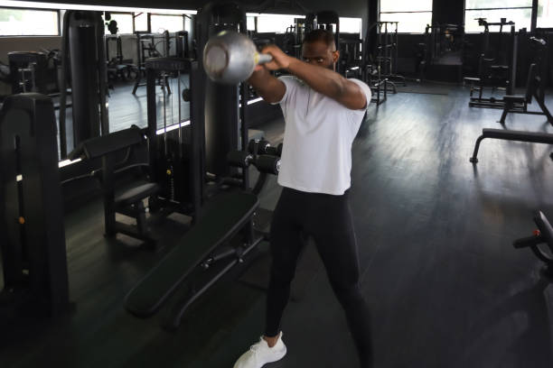 ein fitter und muskulöser afrikanischer mann konzentrierte sich darauf, während eines trainingskurses in einem fitnessstudio eine hantel zu heben. - 16025 stock-fotos und bilder