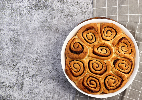 Cinnamon rolls or cinnabon, homemade sweet traditional dessert buns in a white baking dish on a dark grey background. Top view, flat lay