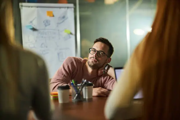 Photo of Bored male freelancer on a meeting with his colleagues in the office.