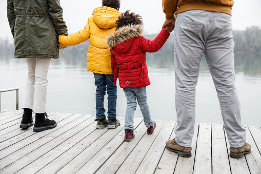 Back view of African American family holding hands on a jetty at river in winter day. Copy space.