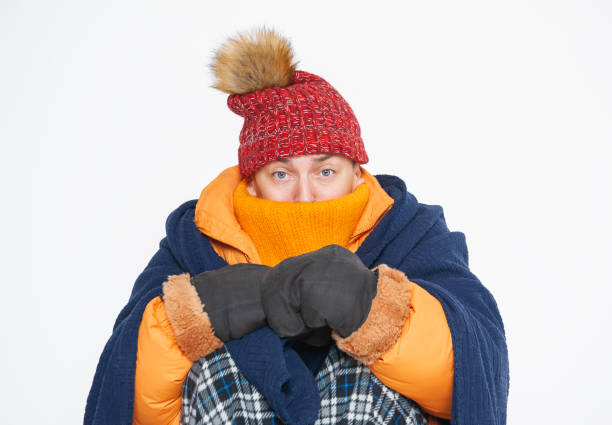 Frightened handsome man wearing in red hat, yellow down jacket and plaid feeling cold sitting on white background. Gas crisis concept