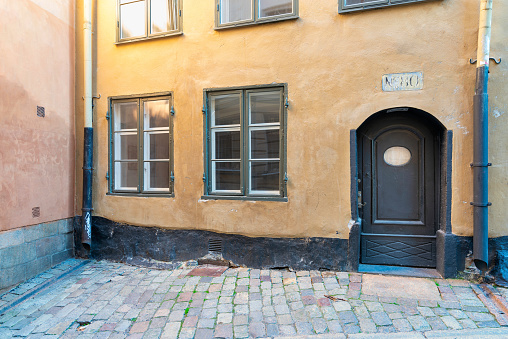 Vintage decorated wooden door, and two wooden windows in a grunge yellow wall at street with cobblestone floor, Old town, Stockholm, Sweden