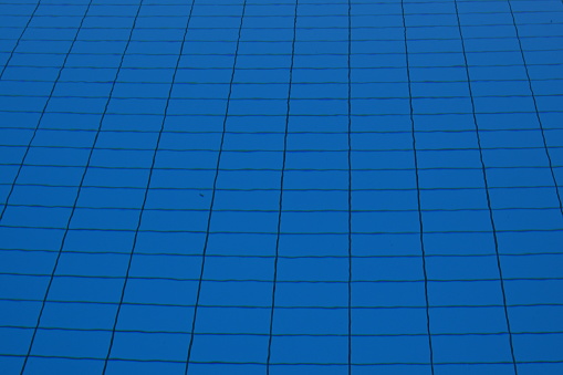 Rectangular tiles on the bottom of a swimming pool full of water in horizontal view. It is a cutout showing the structure  of the tiles. They are of blue color and defocused because of the water.